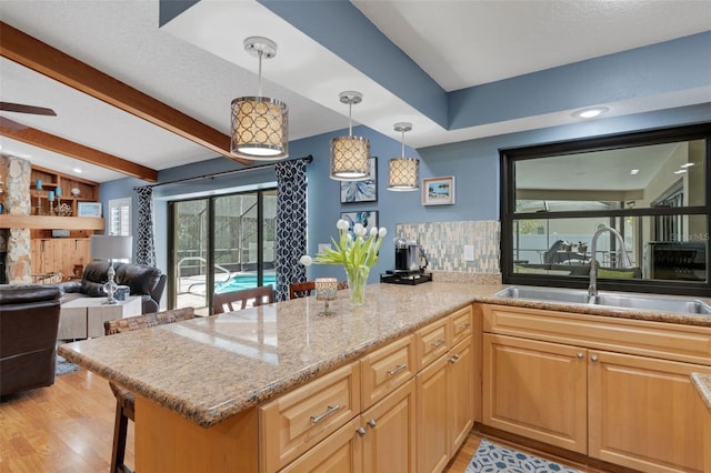 kitchen with beamed ceiling, a peninsula, light stone countertops, light wood-style floors, and a sink