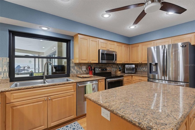 kitchen with light stone counters, a sink, appliances with stainless steel finishes, backsplash, and a center island