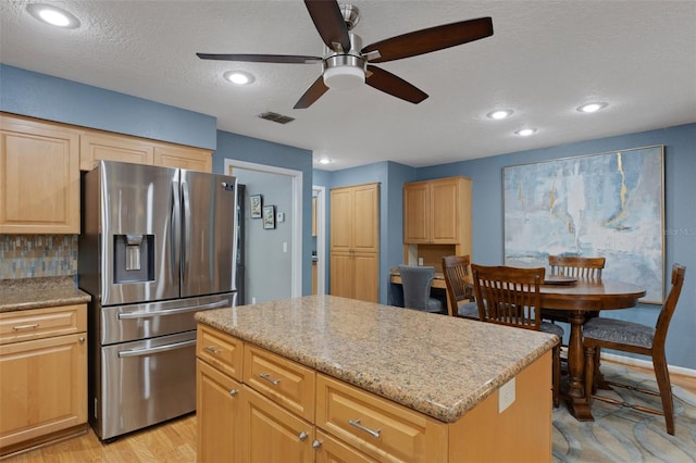 kitchen featuring a center island, visible vents, stainless steel refrigerator with ice dispenser, and light brown cabinetry