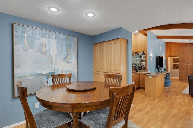 dining space featuring wood walls, light wood-style flooring, a textured ceiling, and beamed ceiling