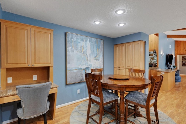 dining area featuring light wood-type flooring, built in study area, a textured ceiling, and baseboards