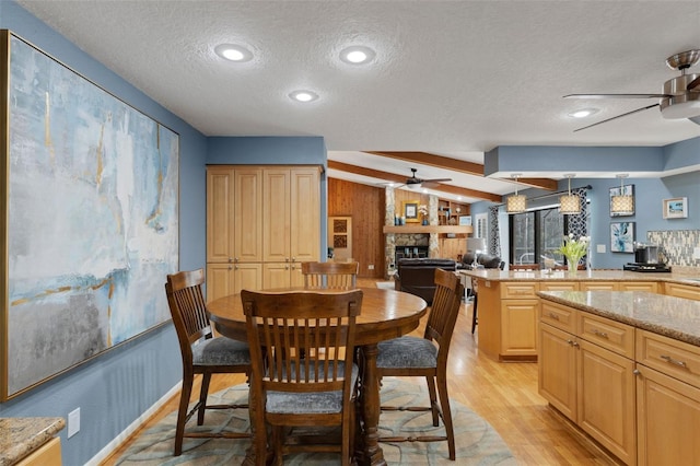 dining area featuring ceiling fan, a stone fireplace, vaulted ceiling, and light wood-style floors