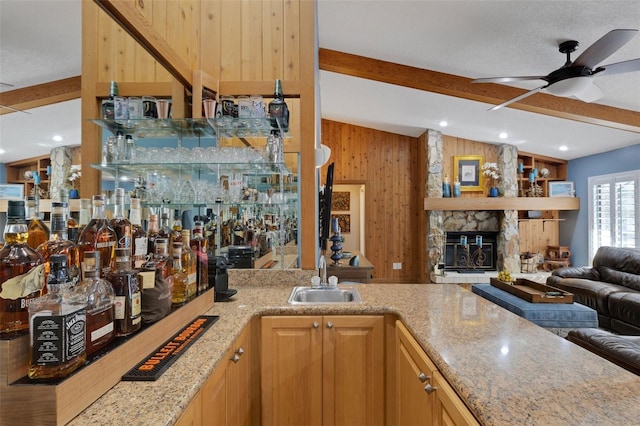 bar featuring lofted ceiling with beams, a sink, wooden walls, a stone fireplace, and wet bar