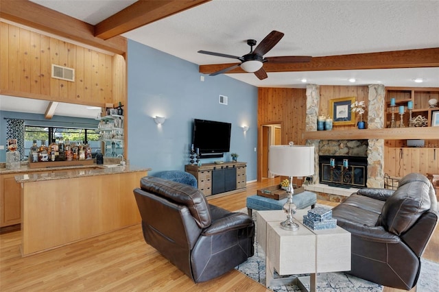 living room with visible vents, a ceiling fan, a textured ceiling, a stone fireplace, and light wood-type flooring