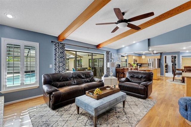 living area featuring lofted ceiling with beams, a textured ceiling, a ceiling fan, baseboards, and light wood finished floors