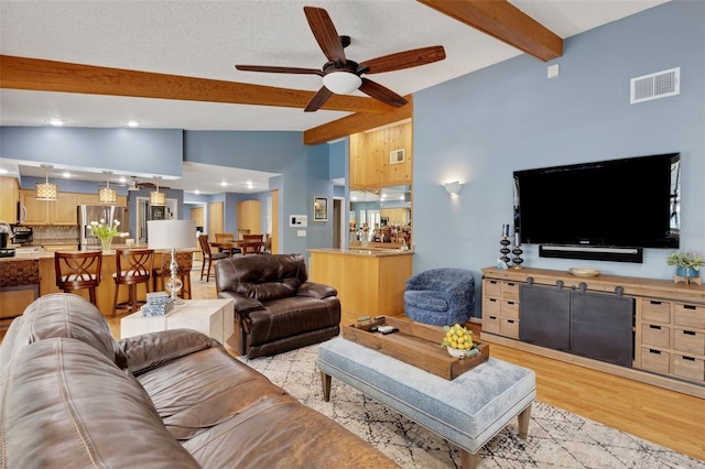 living room with lofted ceiling with beams, a textured ceiling, light wood-style flooring, visible vents, and a ceiling fan