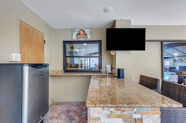 kitchen featuring a peninsula, light stone countertops, a sink, and freestanding refrigerator