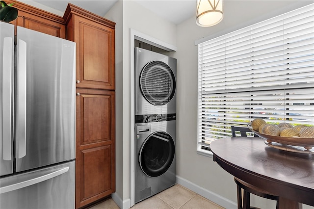 washroom featuring stacked washing maching and dryer, baseboards, light tile patterned floors, and laundry area