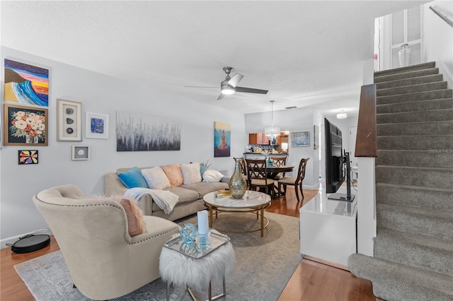 living room featuring baseboards, wood finished floors, stairs, a textured ceiling, and ceiling fan with notable chandelier