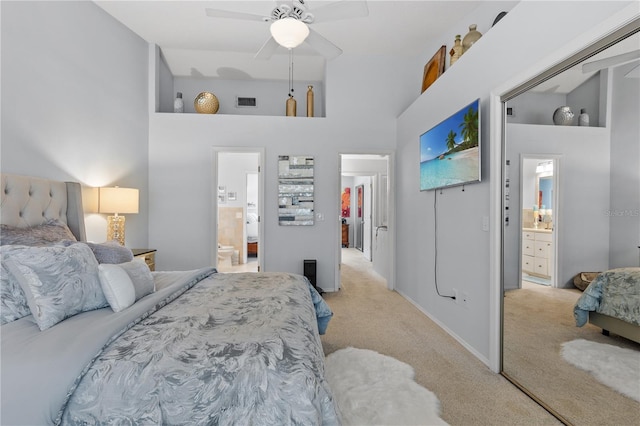 bedroom with ceiling fan, connected bathroom, light colored carpet, visible vents, and a towering ceiling