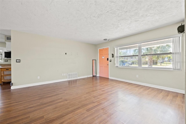 unfurnished living room with a textured ceiling, wood finished floors, visible vents, and baseboards