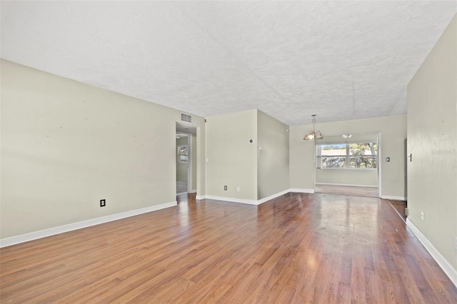 spare room featuring a chandelier, wood finished floors, visible vents, and baseboards