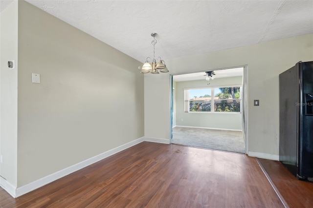 unfurnished dining area featuring an inviting chandelier, a textured ceiling, baseboards, and wood finished floors