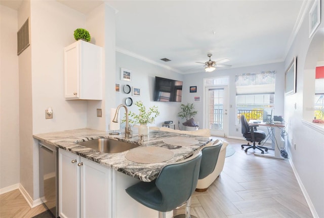 kitchen with a sink, visible vents, white cabinetry, ornamental molding, and light stone countertops