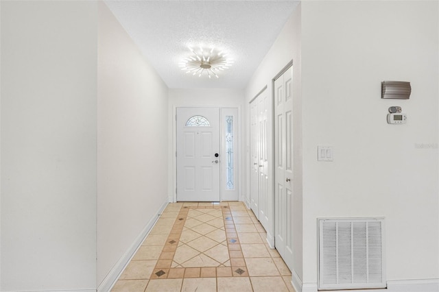 doorway with light tile patterned floors, visible vents, baseboards, and a textured ceiling