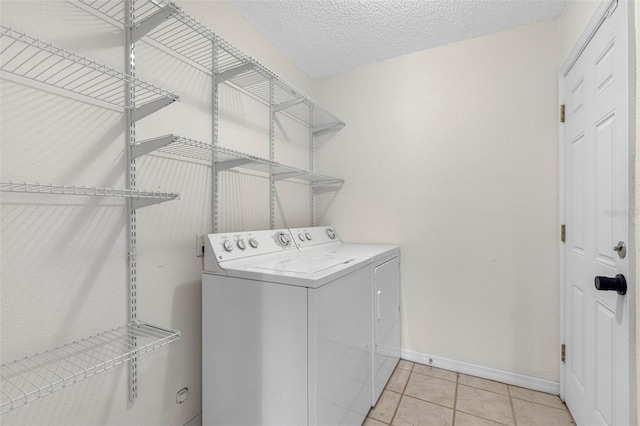 laundry area featuring baseboards, washing machine and clothes dryer, laundry area, light tile patterned flooring, and a textured ceiling