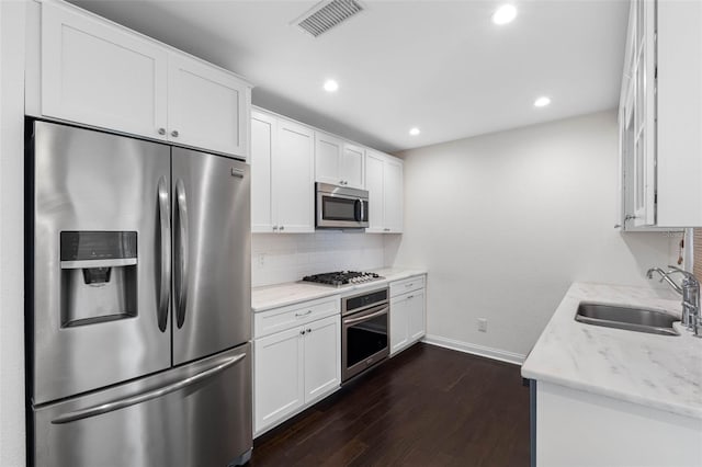 kitchen featuring visible vents, decorative backsplash, dark wood-style floors, stainless steel appliances, and a sink