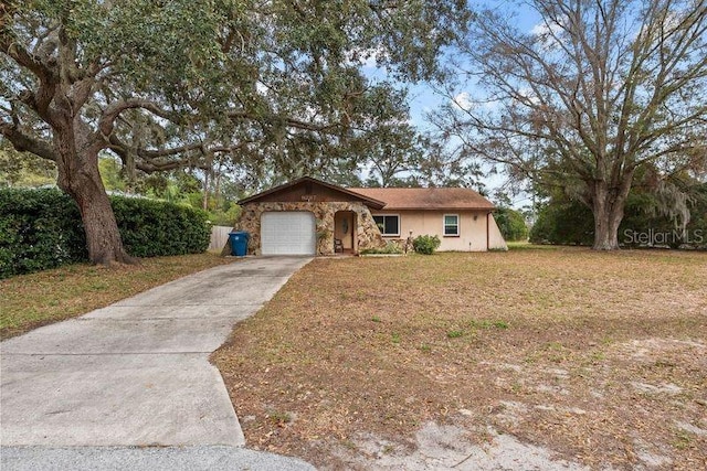 ranch-style house with stucco siding, concrete driveway, a garage, stone siding, and a front lawn