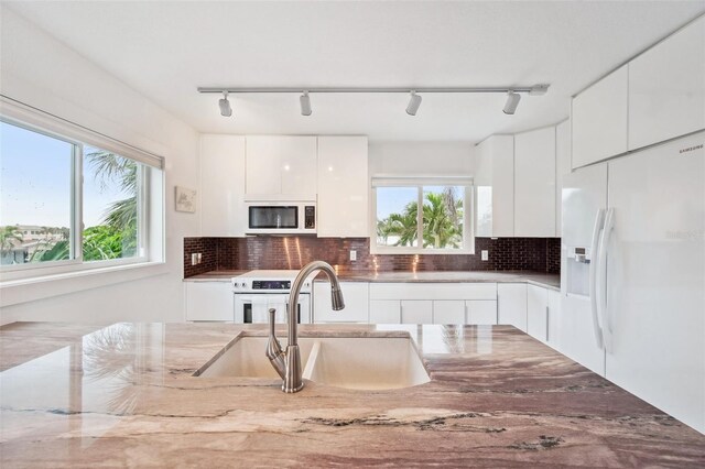 17404 1st St E, Redington Shores, FL 33708 - kitchen featuring white appliances, rail lighting, a sink, modern cabinets, and white cabinets