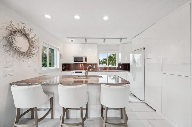 17404 1st St E, Redington Shores, FL 33708 - kitchen featuring white appliances, white cabinetry, plenty of natural light, a kitchen breakfast bar, and recessed lighting