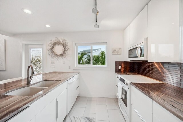 17404 1st St E, Redington Shores, FL 33708 - kitchen with white appliances, a sink, baseboards, decorative backsplash, and white cabinetry