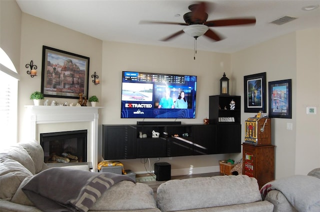 living area featuring visible vents, a ceiling fan, and a glass covered fireplace