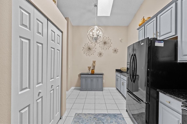 kitchen with light tile patterned floors, dark stone counters, decorative light fixtures, black refrigerator with ice dispenser, and a notable chandelier