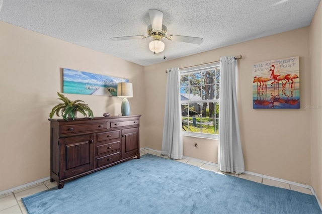 interior space featuring ceiling fan, baseboards, a textured ceiling, and light tile patterned flooring