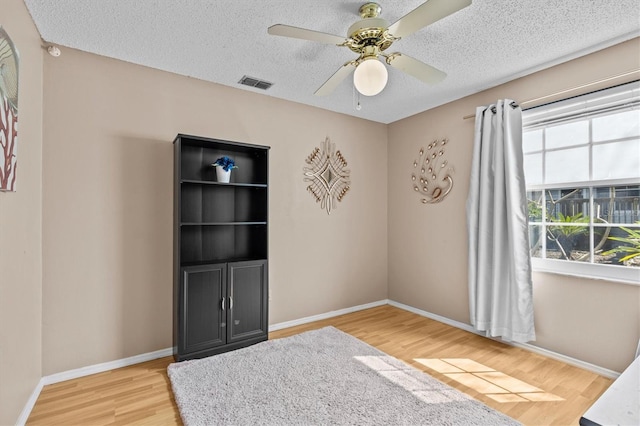 empty room featuring a textured ceiling, wood finished floors, a ceiling fan, visible vents, and baseboards