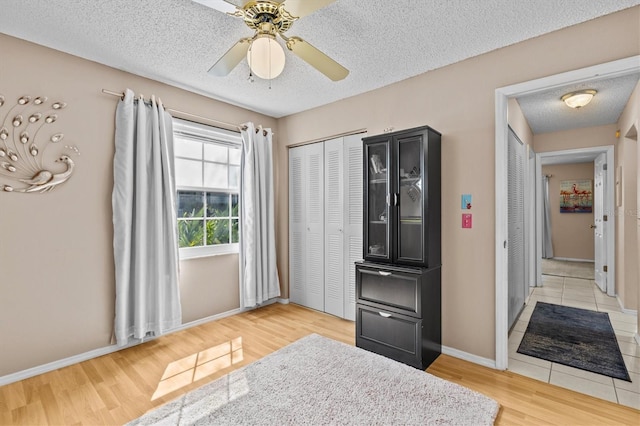 bedroom featuring a closet, ceiling fan, a textured ceiling, light wood-type flooring, and baseboards