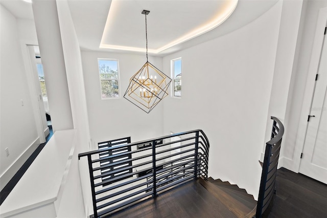 stairs with a raised ceiling, an inviting chandelier, and wood finished floors