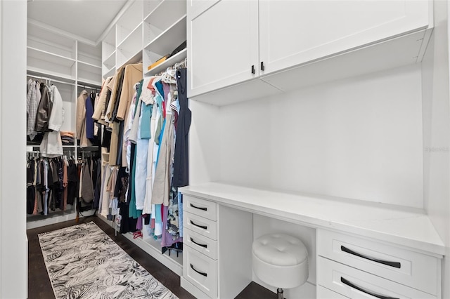 walk in closet with dark wood finished floors and built in study area