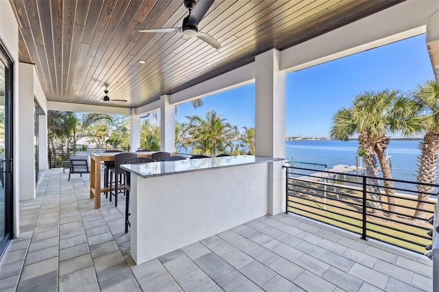 view of patio with a balcony, outdoor wet bar, a ceiling fan, and a water view