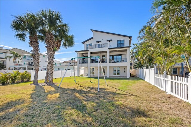 rear view of house featuring a balcony, a fenced backyard, and a lawn