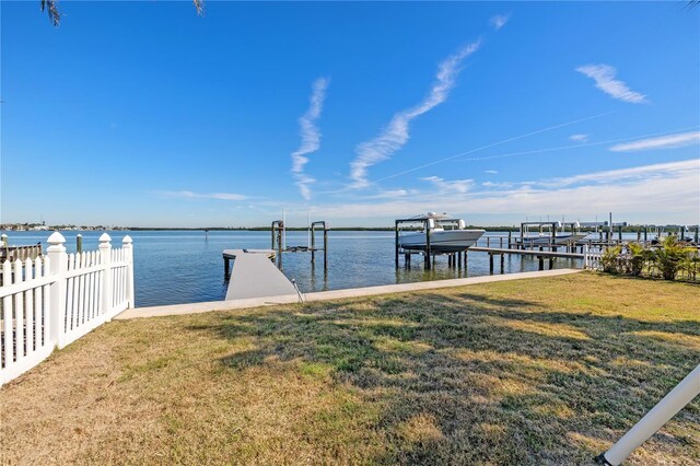 view of dock featuring fence, a lawn, a water view, and boat lift