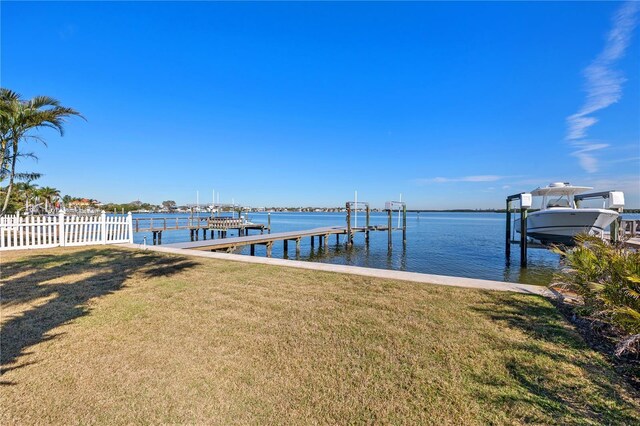 dock area featuring boat lift, a lawn, a water view, and fence