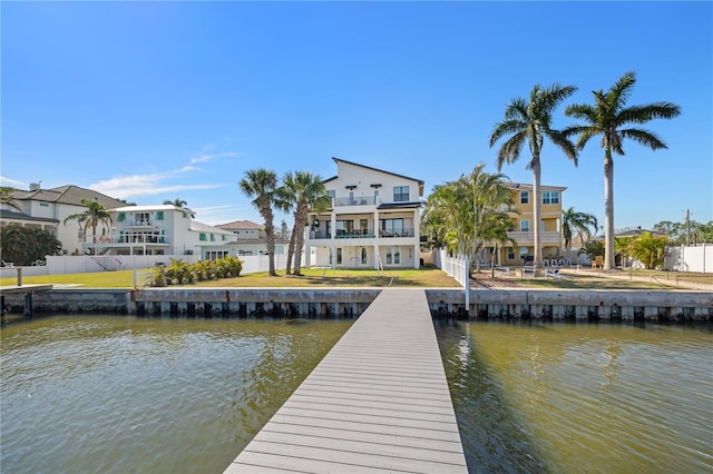 dock area with a balcony, fence, a water view, a lawn, and a residential view