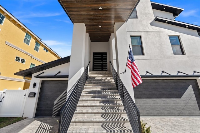 view of exterior entry featuring fence, stucco siding, a gate, and a garage