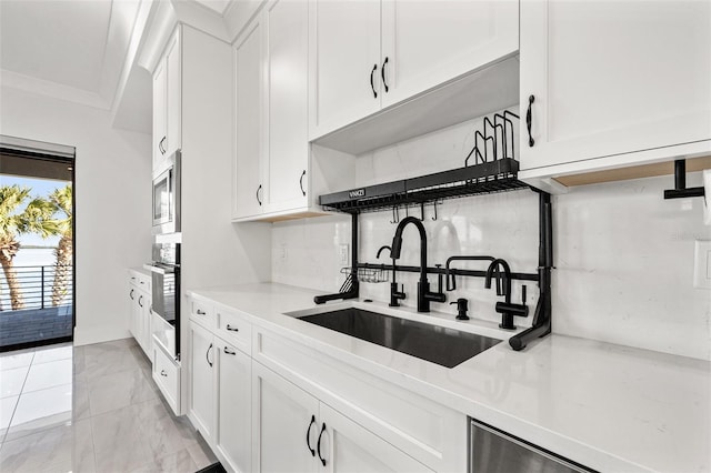 kitchen with appliances with stainless steel finishes, white cabinets, light countertops, and a sink