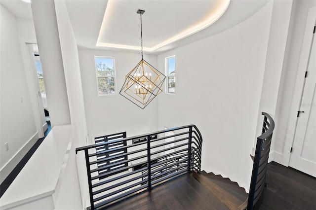 staircase with an inviting chandelier, a raised ceiling, and wood finished floors
