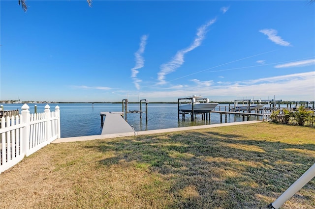 dock area featuring a water view, fence, boat lift, and a yard