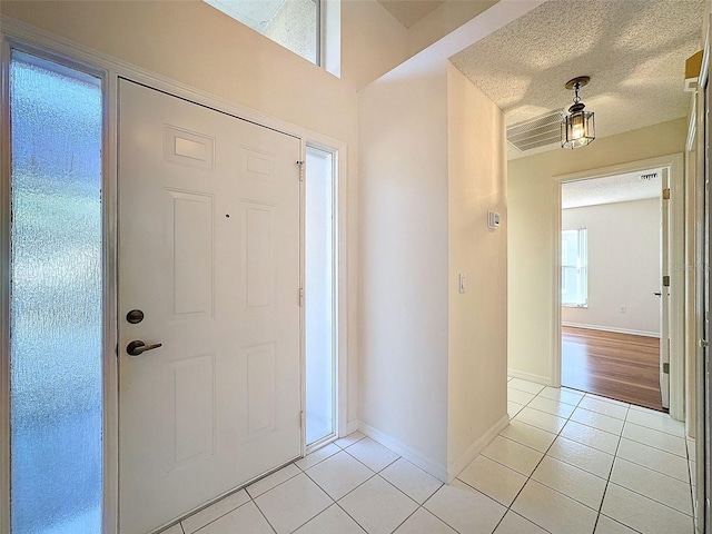 entryway with light tile patterned floors, a textured ceiling, and baseboards