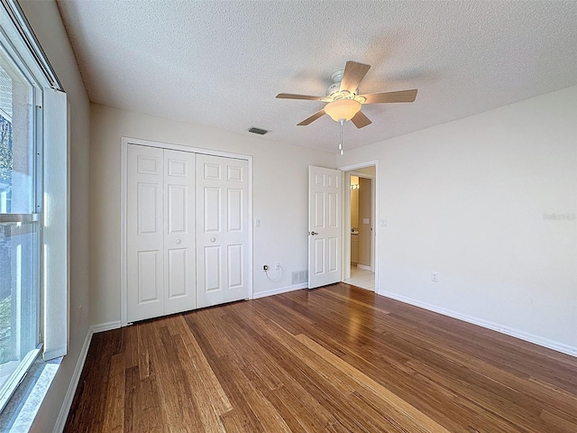 unfurnished bedroom with baseboards, visible vents, wood finished floors, a textured ceiling, and a closet