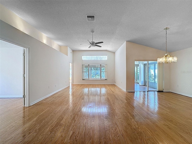 empty room with visible vents, vaulted ceiling, a textured ceiling, wood finished floors, and ceiling fan with notable chandelier