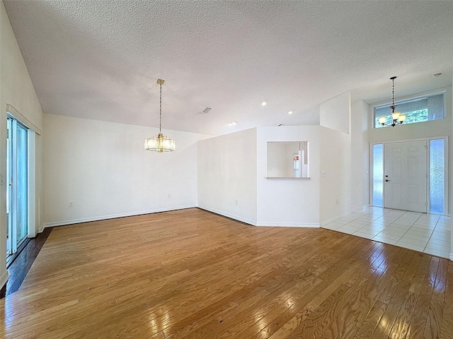 interior space featuring a chandelier, a textured ceiling, visible vents, baseboards, and light wood-type flooring