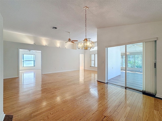 unfurnished room with ceiling fan with notable chandelier, a textured ceiling, light wood-type flooring, and visible vents