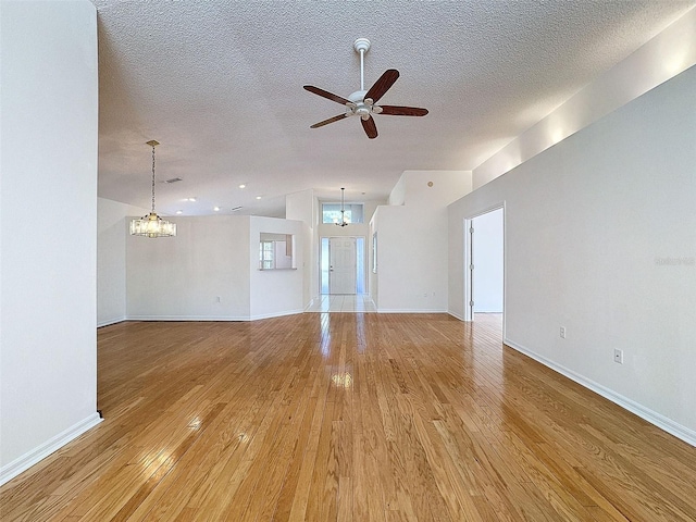 unfurnished living room with baseboards, a textured ceiling, light wood finished floors, and ceiling fan with notable chandelier