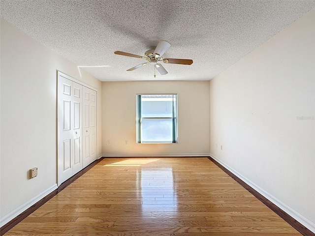 unfurnished bedroom with a textured ceiling, a closet, wood finished floors, and baseboards