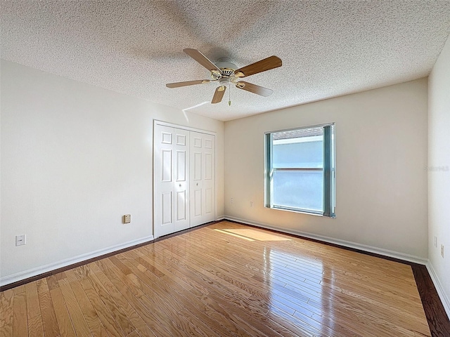 unfurnished bedroom featuring a closet, wood-type flooring, a ceiling fan, a textured ceiling, and baseboards