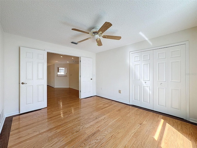 unfurnished bedroom featuring light wood finished floors, a closet, visible vents, a textured ceiling, and baseboards